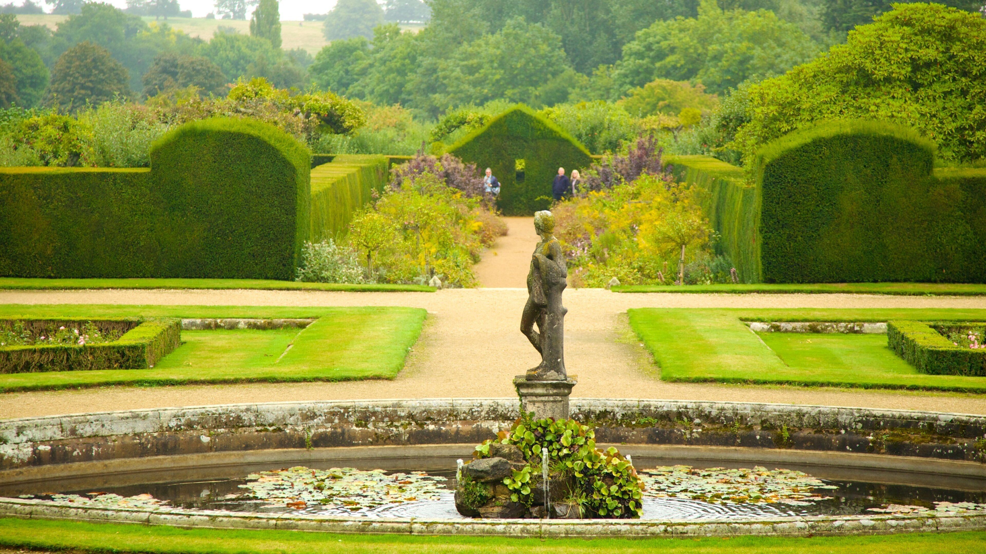 A formal garden with a statue, neatly trimmed hedges, and a pond with lily pads.