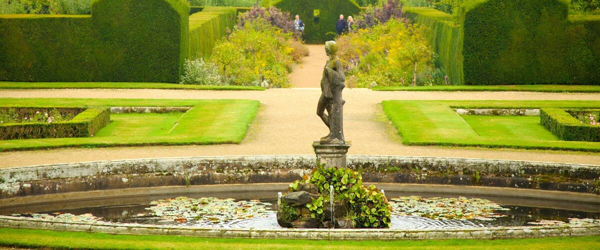 A formal garden with a statue, neatly trimmed hedges, and a pond with lily pads.