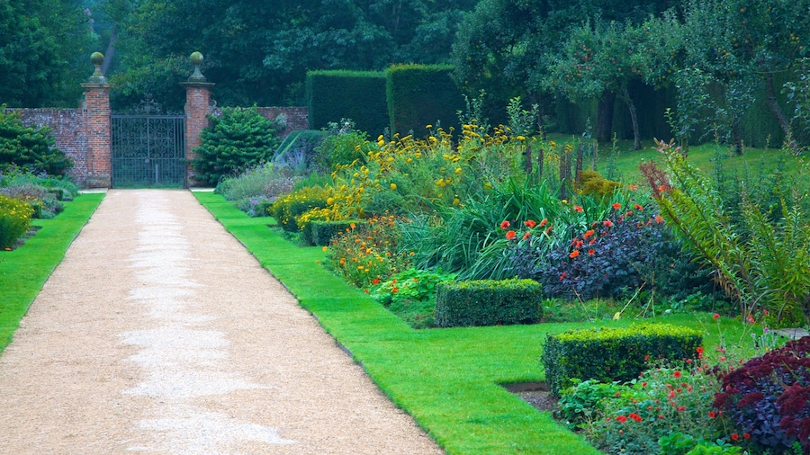 A garden pathway leading to a brick gate, surrounded by well-manicured hedges and colorful flowers.