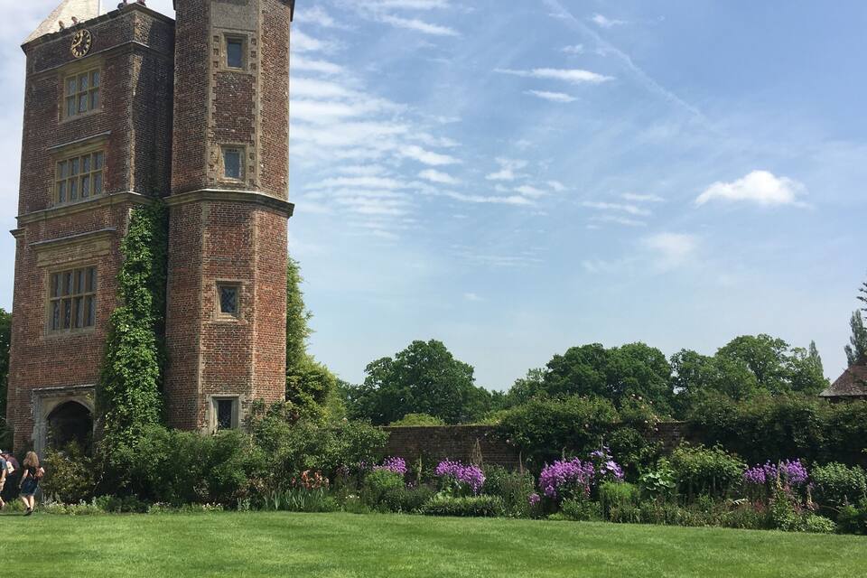 A historic brick tower with a clock, surrounded by lush green grass and purple flowers.