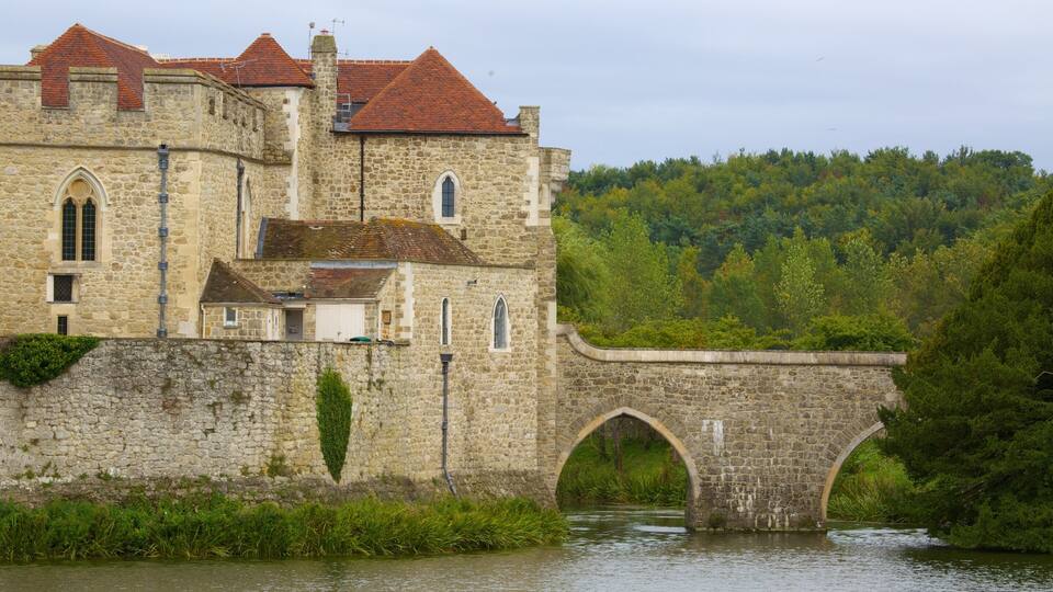A historic stone building with a red-tiled roof, a stone bridge, and a forested hillside.