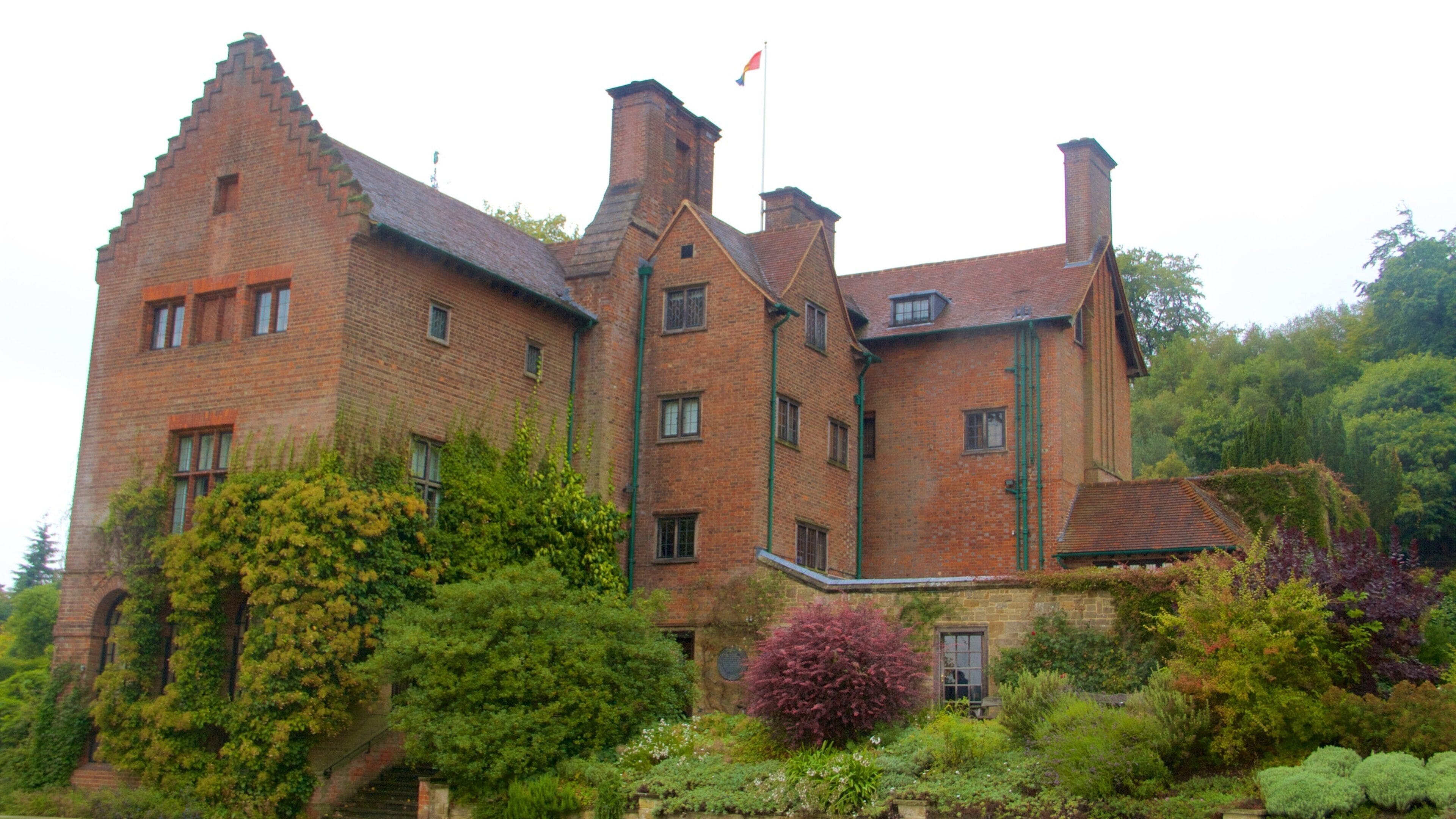 A large brick building with a flag, surrounded by lush greenery and trees.