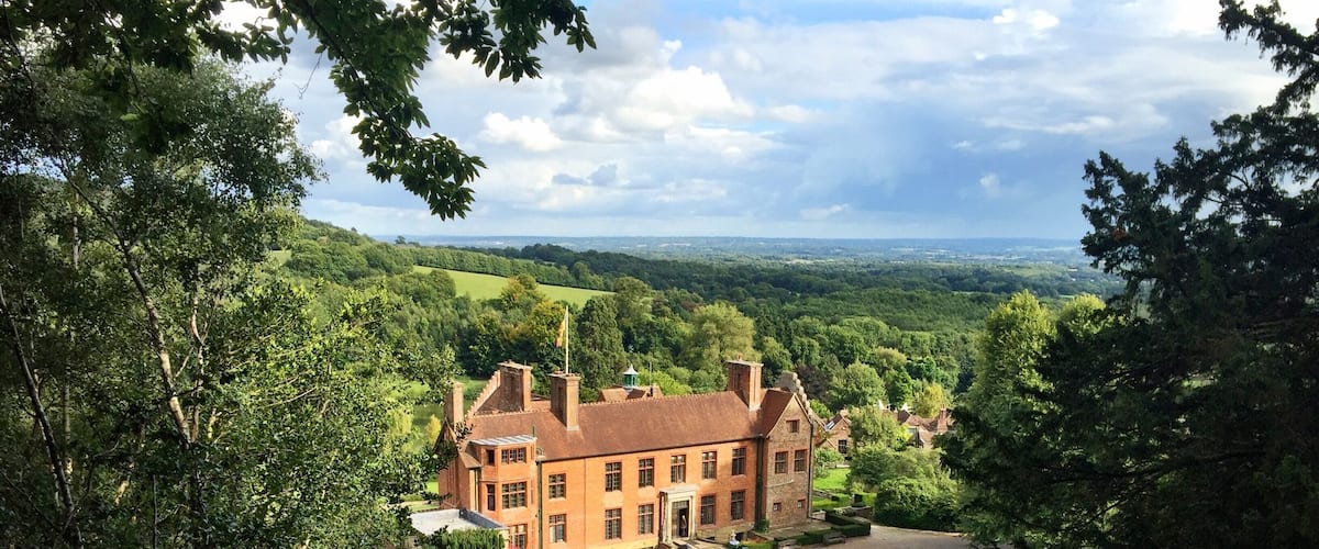 A large brick manor surrounded by lush greenery and a winding road.