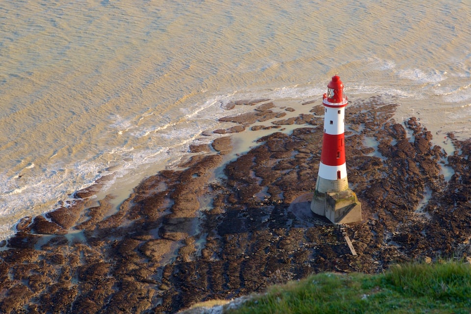 A red and white lighthouse on a rocky shore with waves crashing nearby.