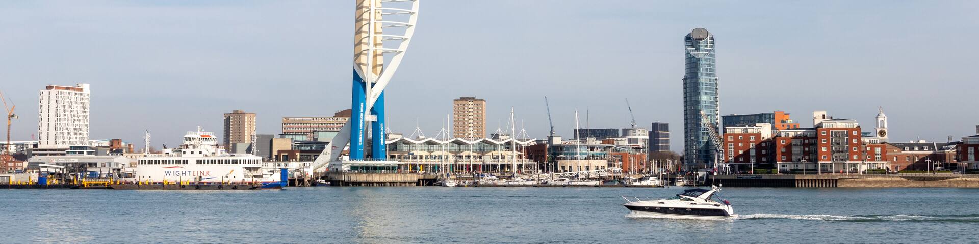 A modern sail-shaped building, a marina with boats, and a city skyline with various buildings.