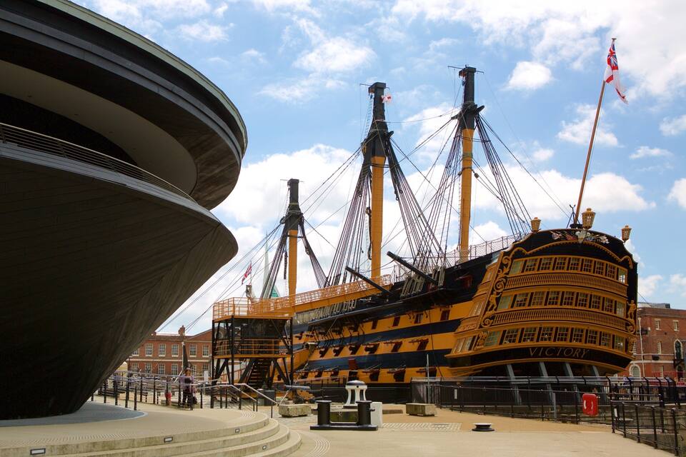 A historic ship docked at a waterfront, with a large modern structure in the foreground.