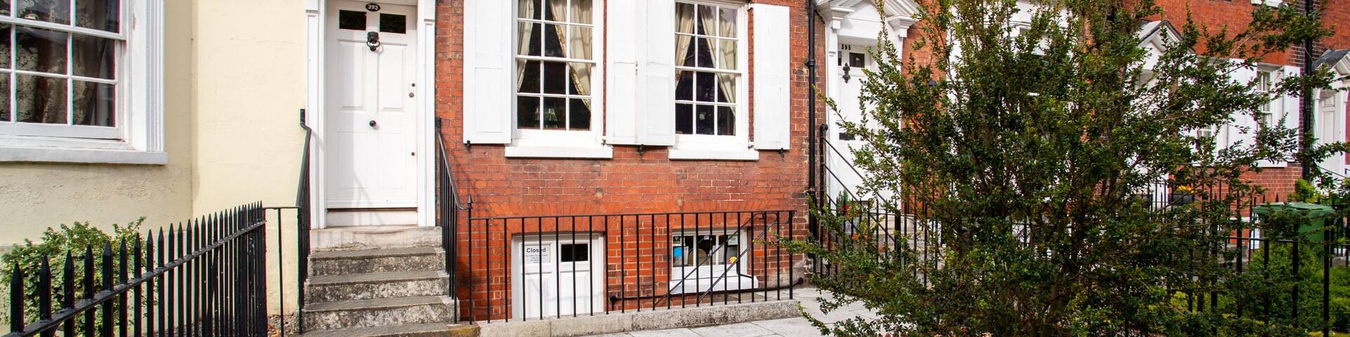 A red brick house with white shutters, a white door, and a small garden with red flowers.
