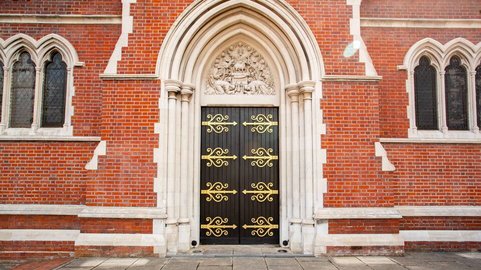 A red brick building with a black door featuring gold decorative elements and a stone archway above it.