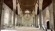 A cathedral interior with high vaulted ceilings, large stained glass windows, and a prominent circular stained glass window at the center.