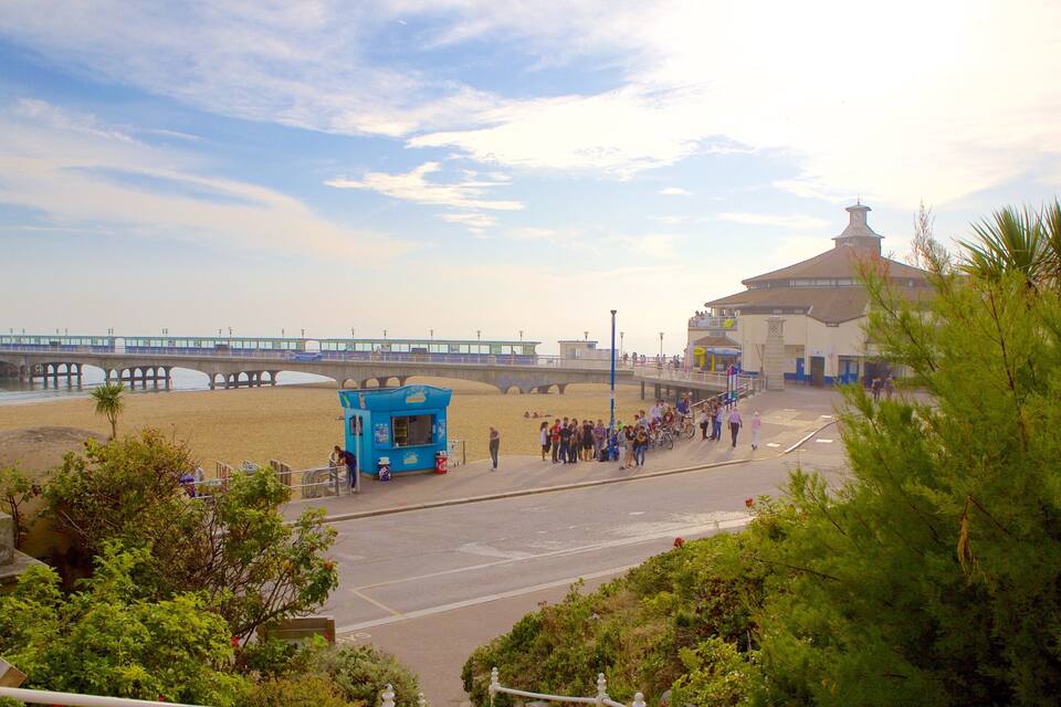 A beach with a pier, a blue kiosk, and a building with a clock tower.