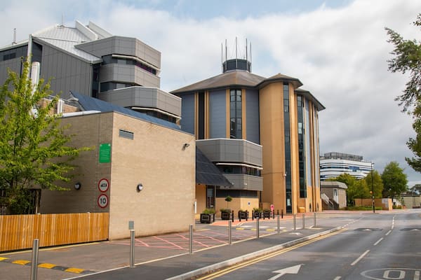 A modern building with a mix of brick and glass facades, a curved structure, and a flat roof with solar panels.