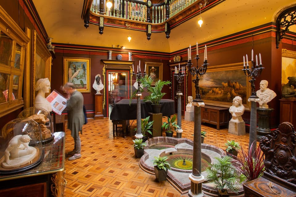 An ornate room with a wooden parquet floor, classical sculptures, and a central fountain.