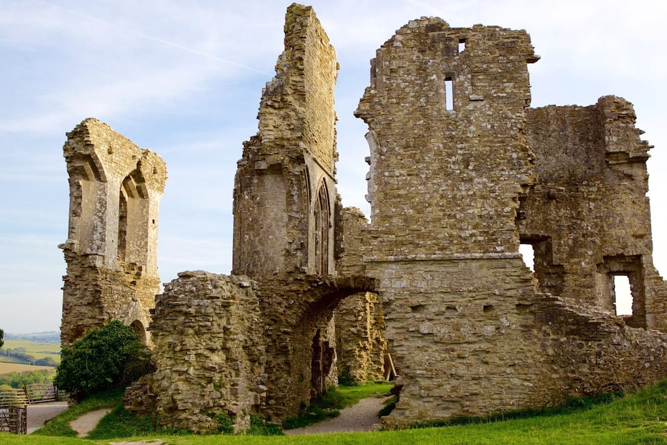 The ruins of a medieval stone structure with arches and towers, surrounded by greenery.
