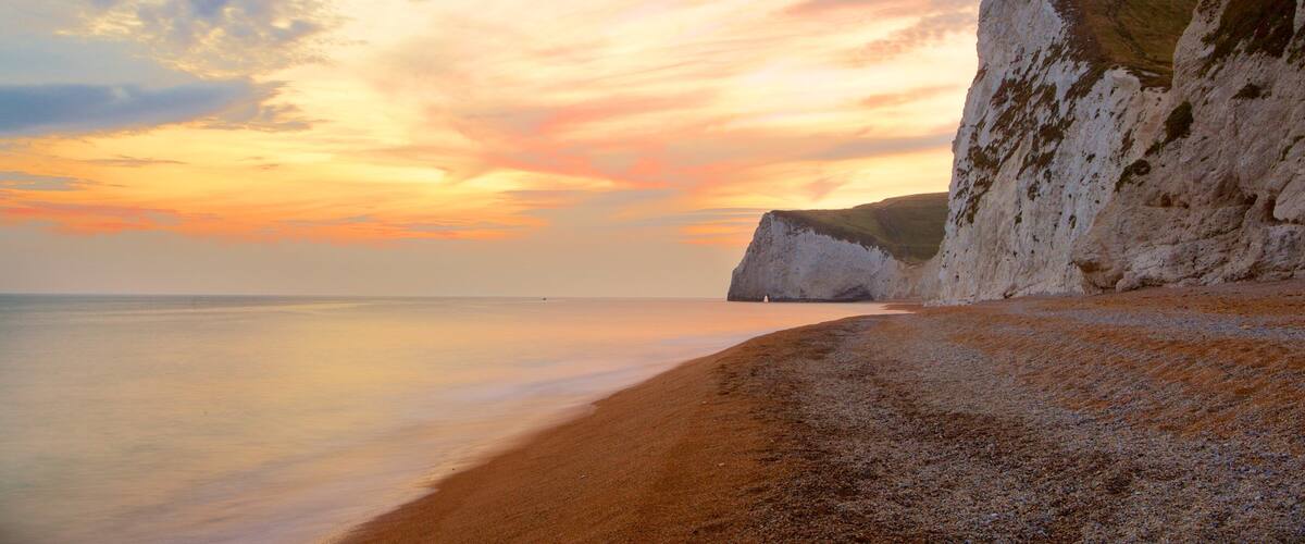A beach with white cliffs and a sunset.