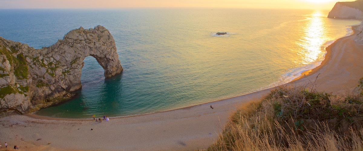 Durdle Door ofreciendo costa rocosa, una puesta de sol y una bahía o puerto