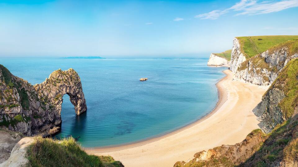 A coastal landscape with a prominent rock arch formation, a sandy beach, and a cliffside.