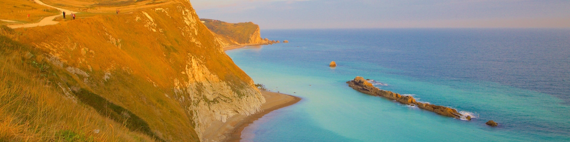 Paisagem costeira com falésias, uma praia e uma formação rochosa na água.