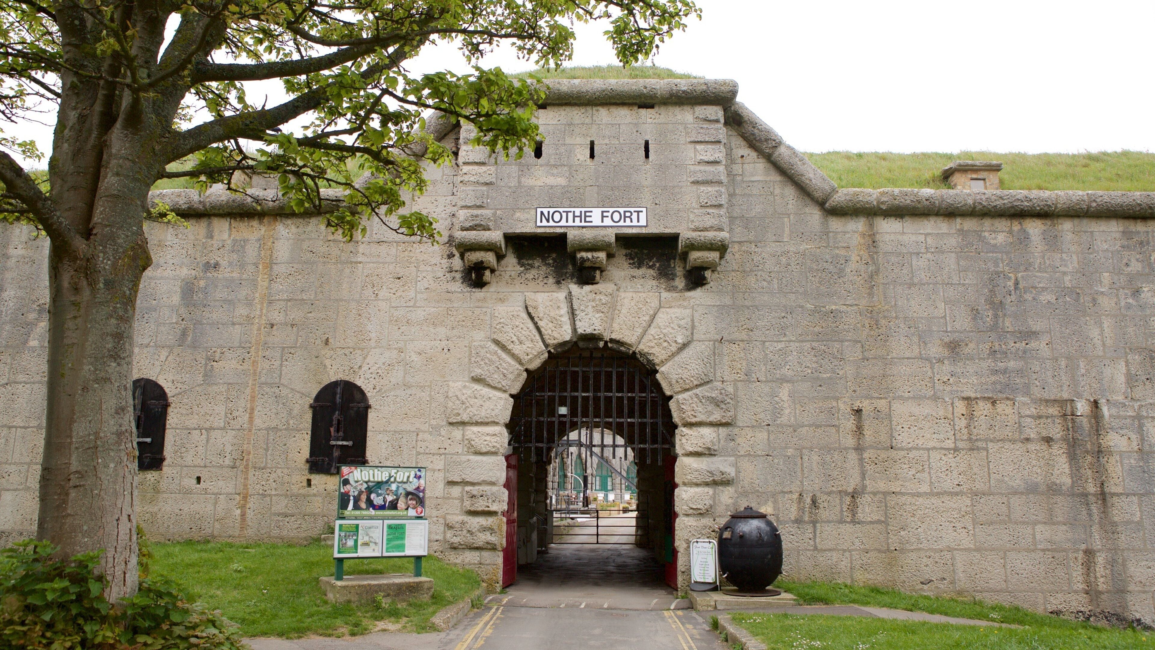 The entrance to Nothe Fort with a stone wall, a gate, and a signboard.