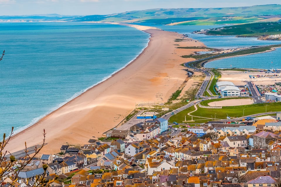 A coastal town with a sandy beach, a blue sea, and a dense cluster of colorful houses.