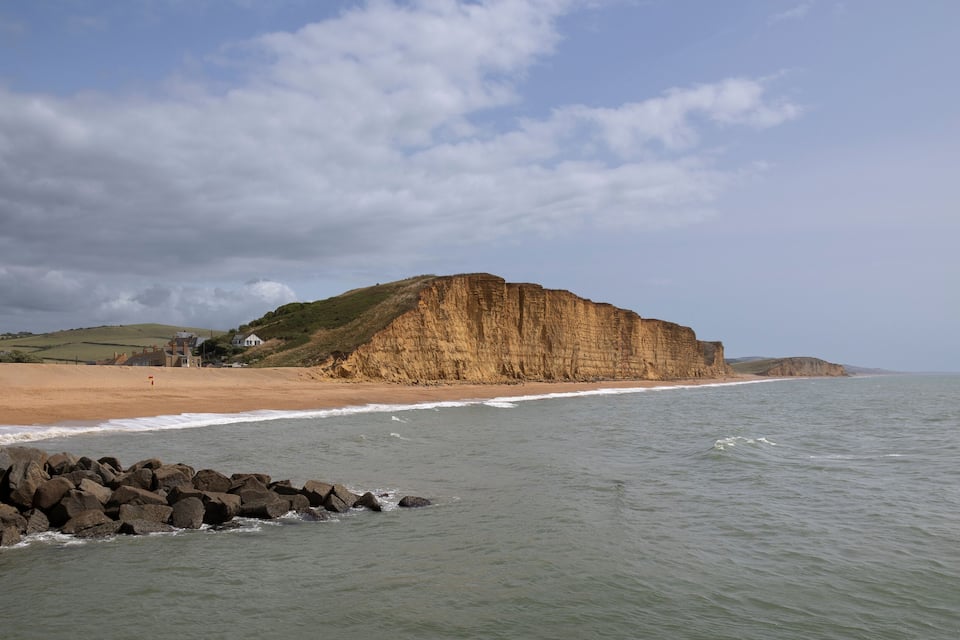 Un paysage côtier caractérisé par une falaise imposante, une plage de sable et une côte rocheuse.