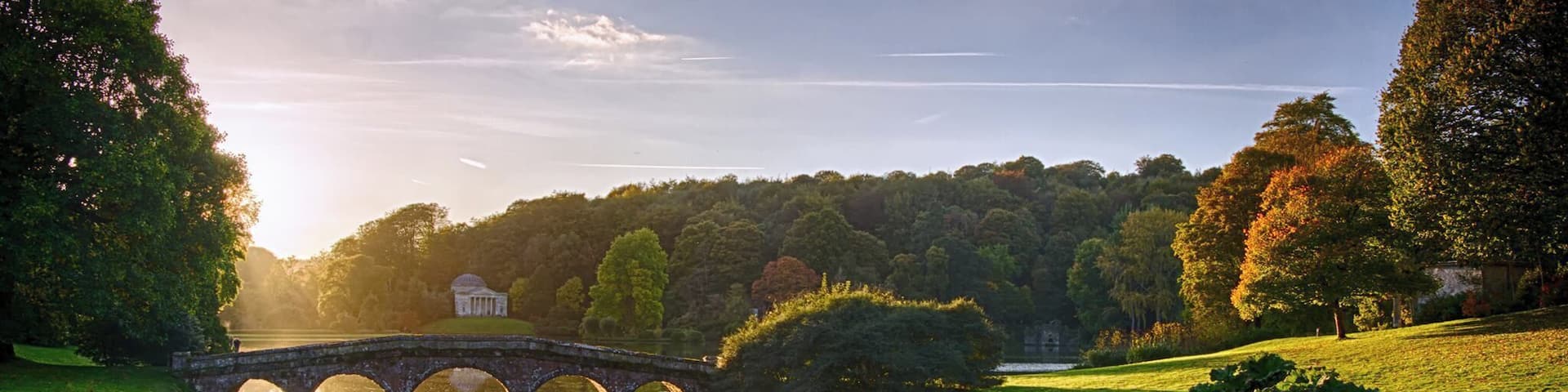 A stone bridge over a calm river, surrounded by lush greenery and trees.