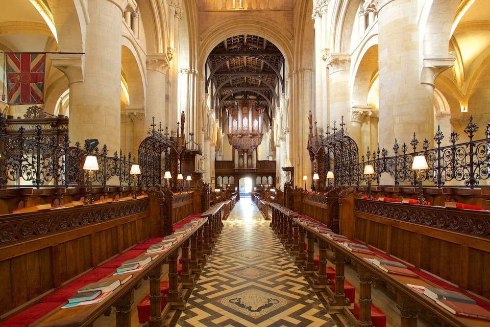 Een kerkinterieur met houten banken, een versierd vloertapijt en een groot orgel vooraan.