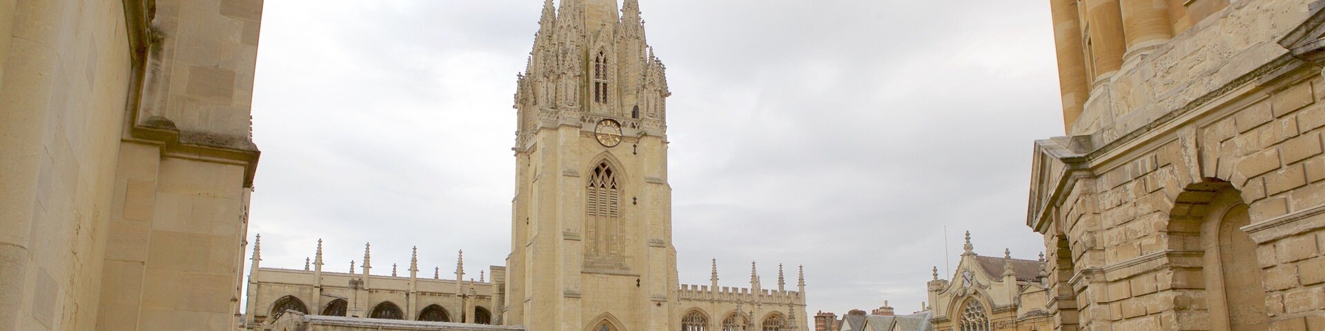 Uma catedral histórica com uma torre alta, rodeada por edifícios de pedra e uma rua com pedestres e bicicletas.