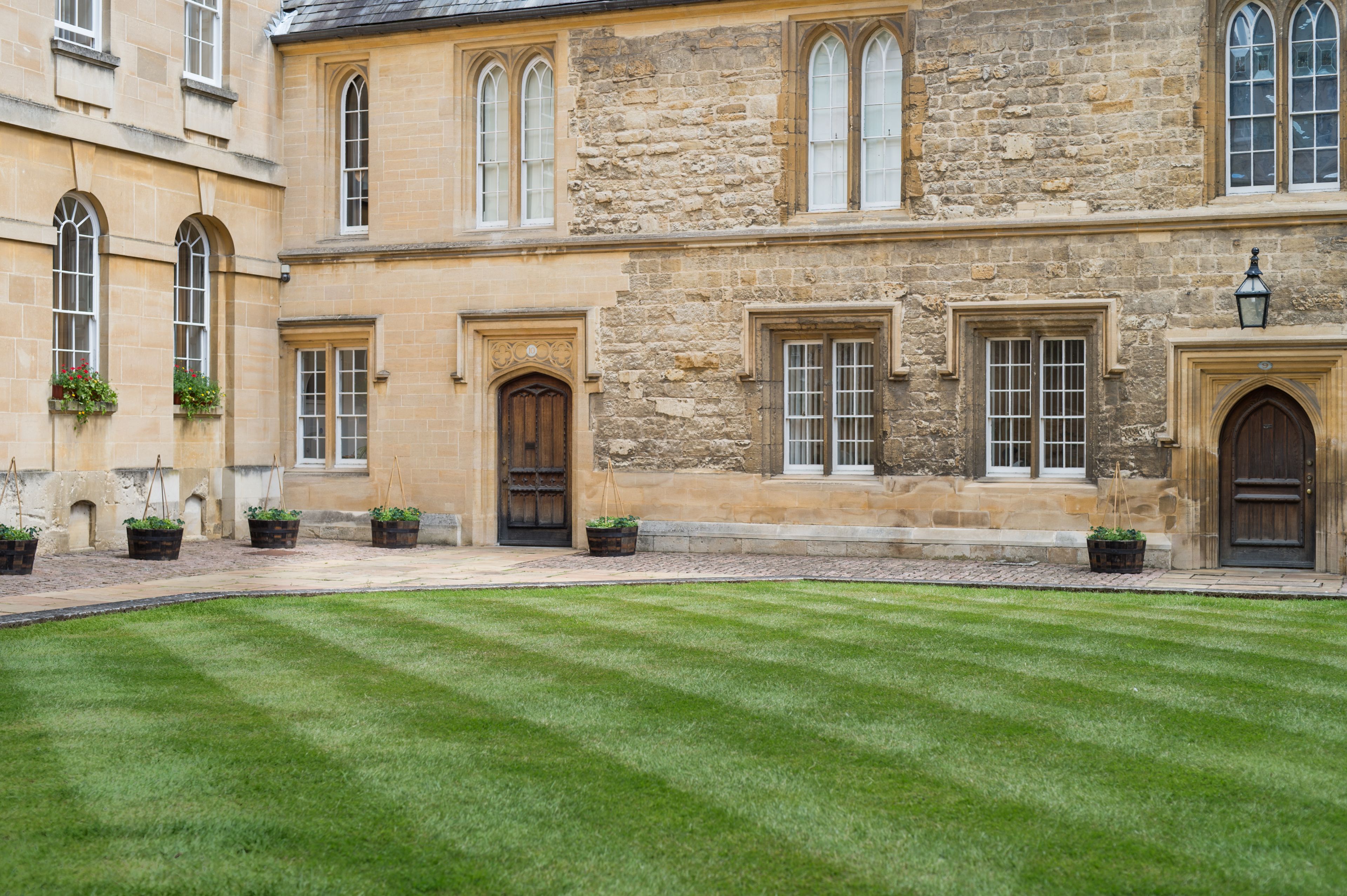 A historic stone building with arched windows and doors, a well-manicured lawn, and flower boxes.