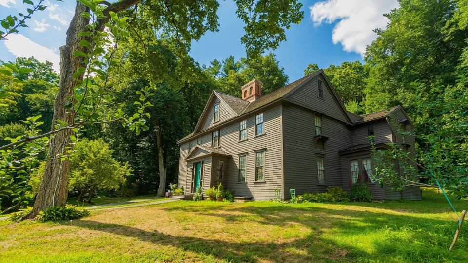A two-story house with a brick chimney, surrounded by lush green trees and a well-maintained lawn.