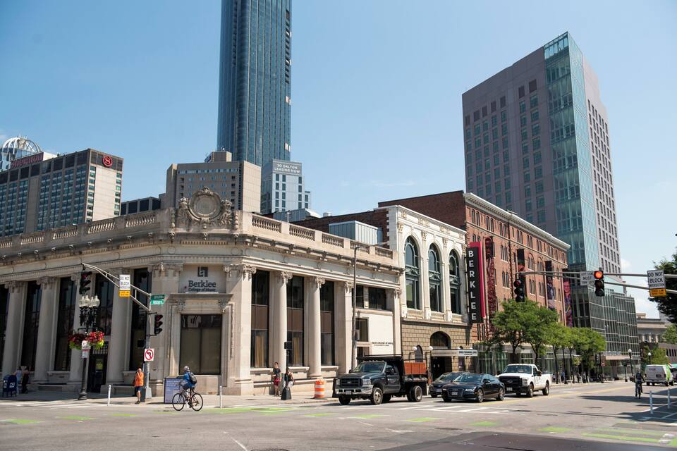 A city street with tall buildings, including a historic building with columns and a modern glass skyscraper.