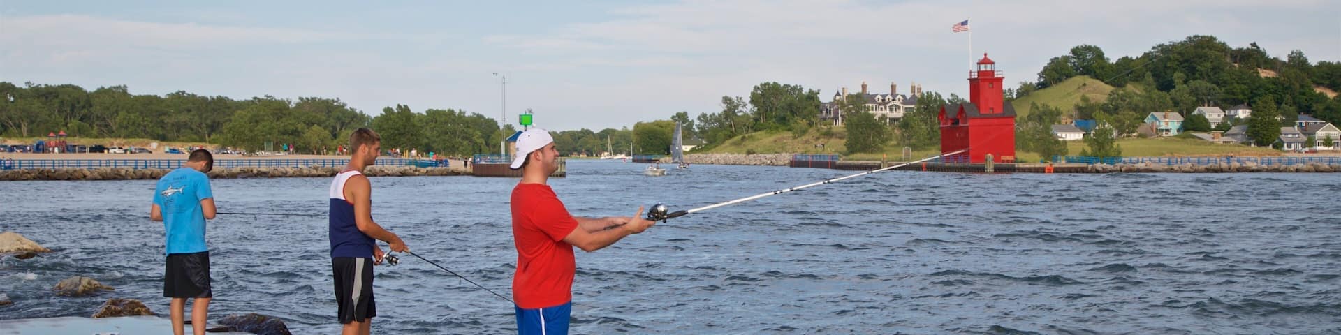 Three people fishing by a waterfront with a red lighthouse in the background.