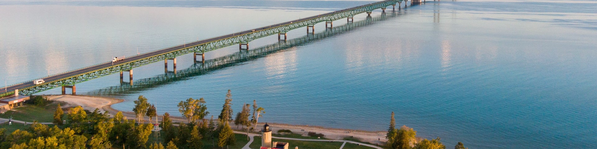 Aerial view of the Mackinac Bridge over calm waters in the morning, with view of the Old Mackinac Lighthouse