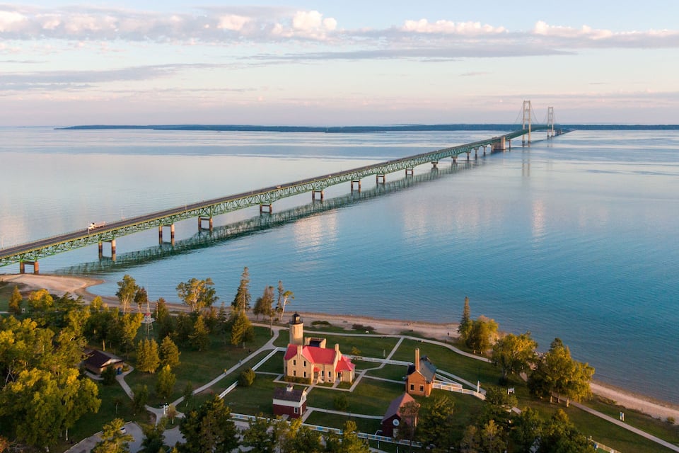 A long bridge spanning a calm body of water, with a park and buildings in the foreground.
