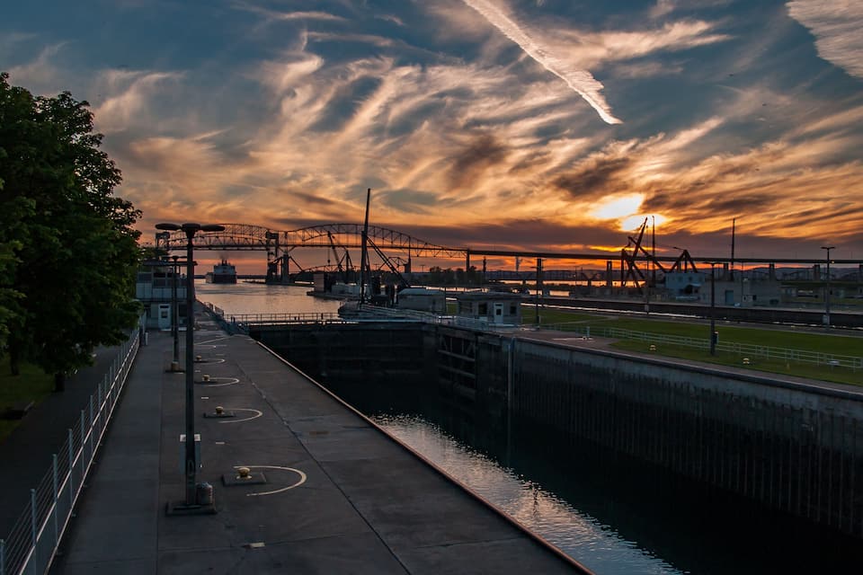 A sunset over a harbor with a bridge and industrial structures.