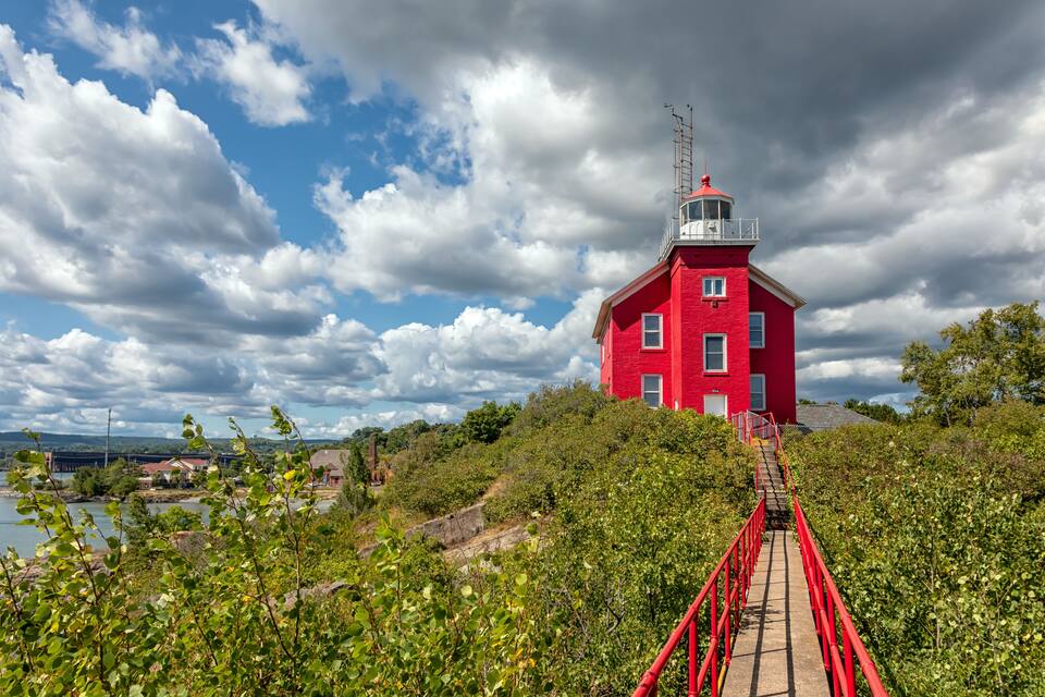 Un faro rojo sobre un puente, rodeado de vegetación.