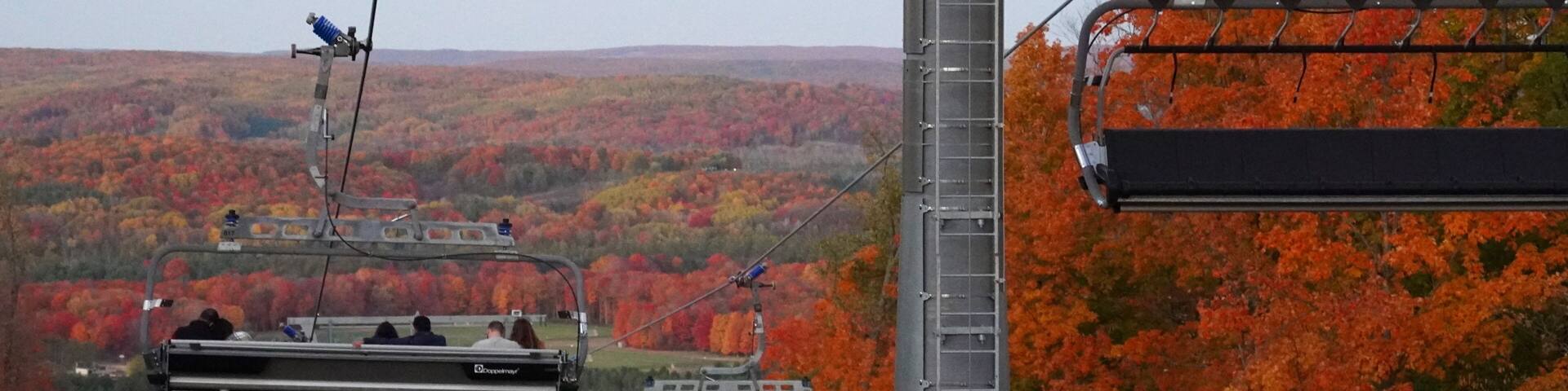 A cable car system with passengers, set against a backdrop of autumn-colored trees.