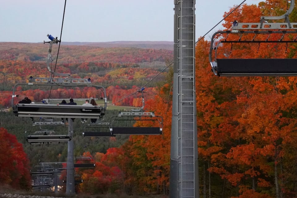 A cable car system with passengers, set against a backdrop of autumn-colored trees.