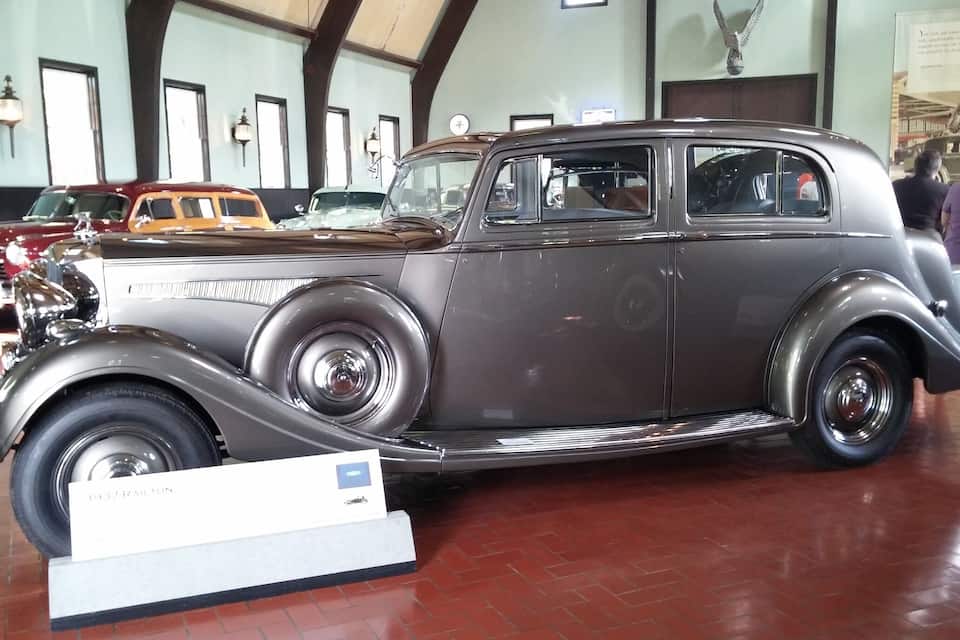 Een oldtimer in een museum, met stenen vloer en andere klassieke auto's op de achtergrond.