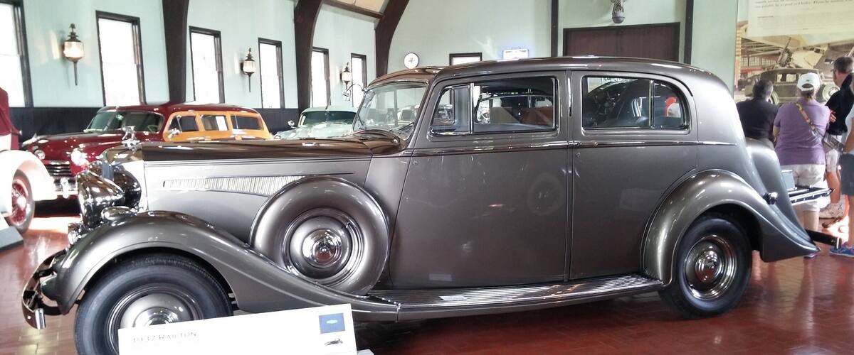 A vintage car on display in a museum with brick flooring and other classic cars in the background.