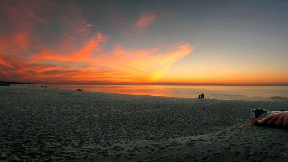 A beach at sunset with a colorful sky, footprints, and kayaks.