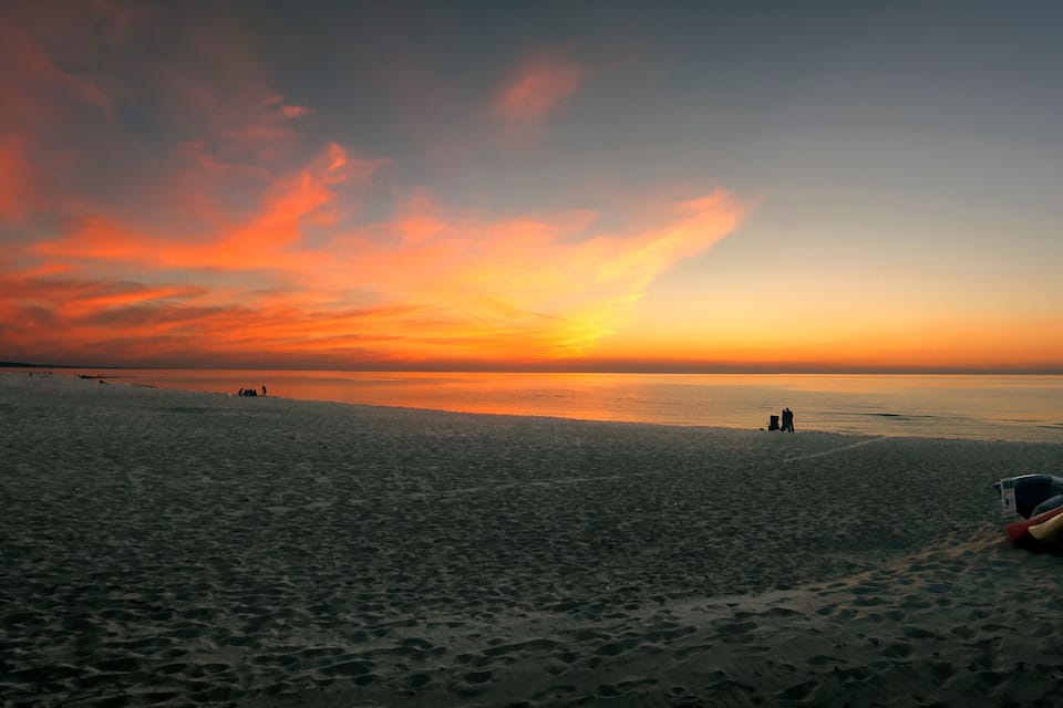A beach at sunset with a colorful sky, footprints, and kayaks.