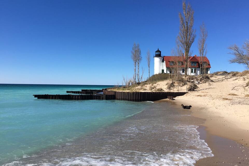 Una playa con un faro y una casa en una duna arenosa.