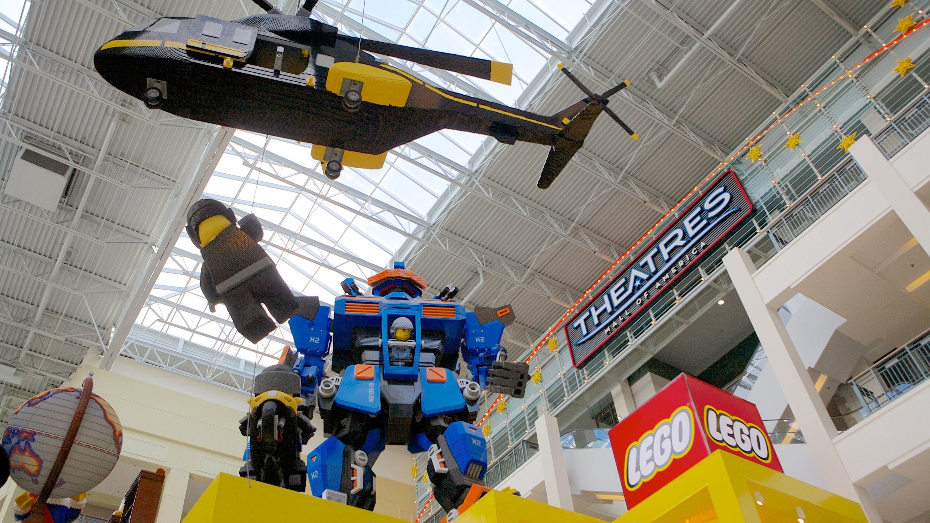 Una gran exposición en interiores que muestra piezas de LEGO, incluyendo un helicóptero y un robot.