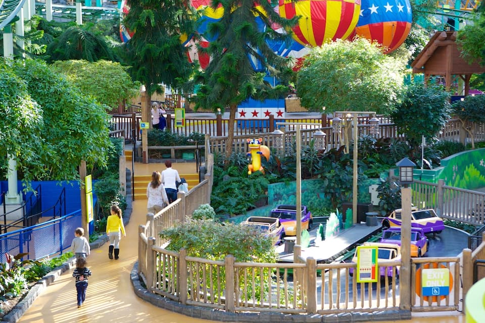 Un parque temático con un puente de madera, globos aerostáticos y un carrusel.