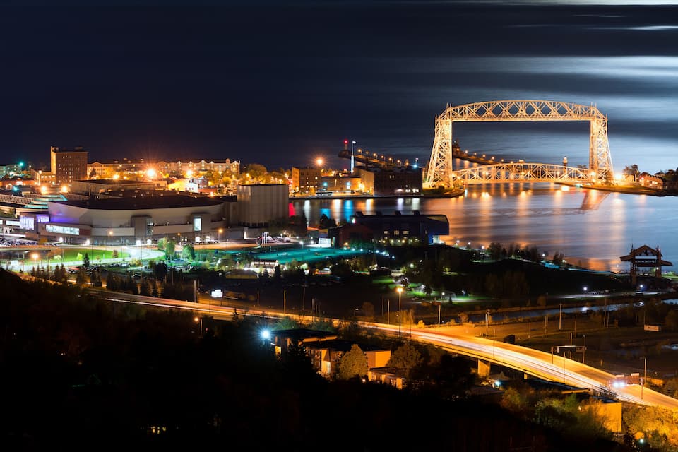 A nighttime cityscape with a prominent bridge, illuminated buildings, and a river.