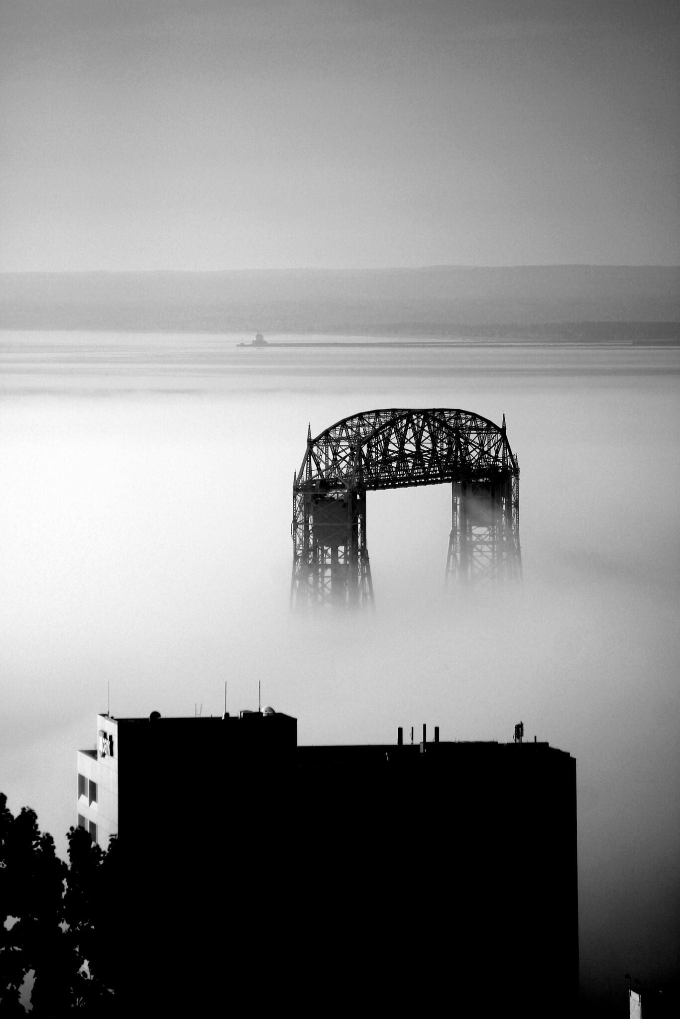 Lift bridge appears above the early morning fog. Wisconsin point lighthouse stands on the horizon. #Trovember