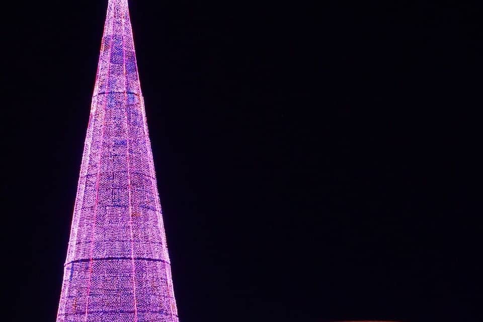 A large illuminated Christmas tree with a star on top, surrounded by festive lights and decorations.