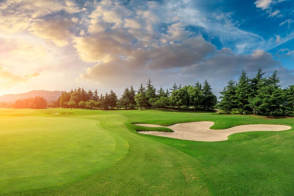 A golf course with a sand bunker, trees, and a mountain in the background.