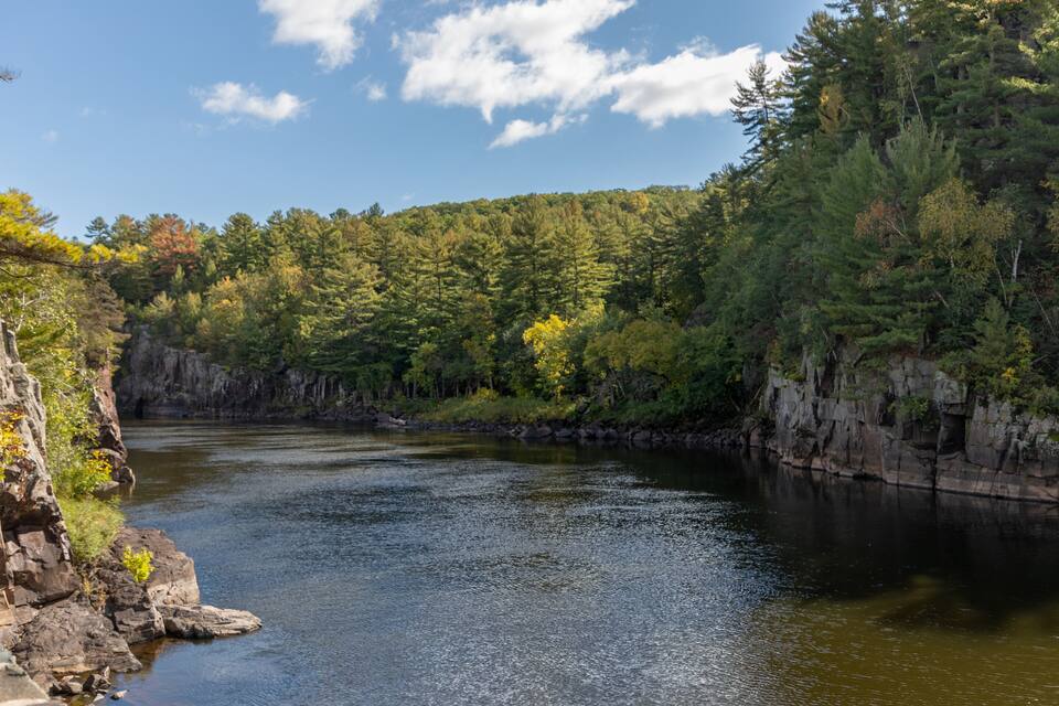 A river flowing through a forested valley with rocky cliffs on one side.