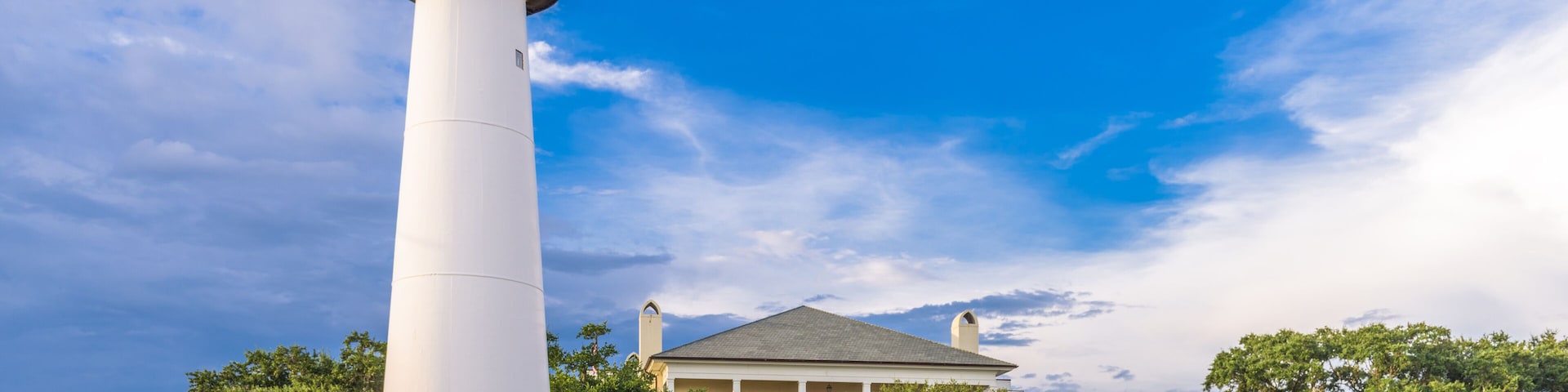 A white lighthouse, a large house with a porch, and lush green trees.